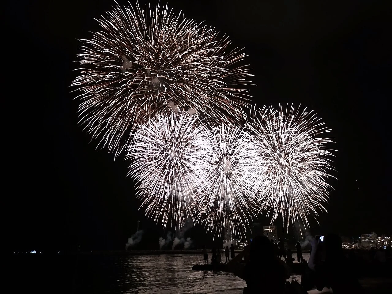 熱海海灣上空綻放的海上花火,近岸可見觀賞人群與水面