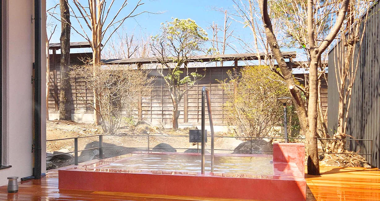 如心之里（ひびき）野露天黃金之湯，紅褐色浴池位於庭園樹木旁